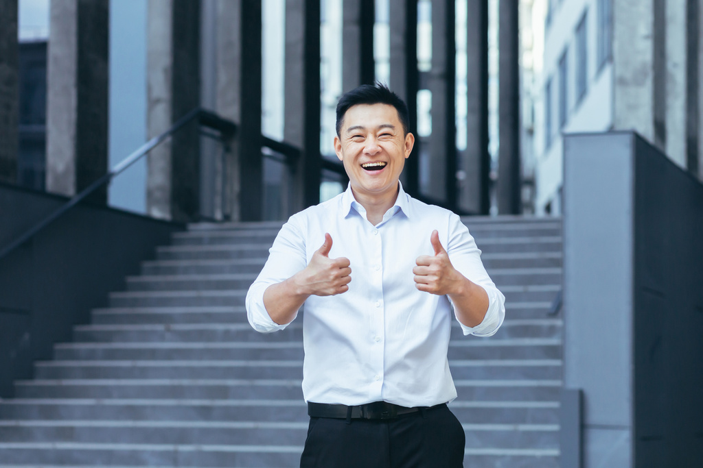 Successful asian businessman outside office smiling, thumbs up affirmatively